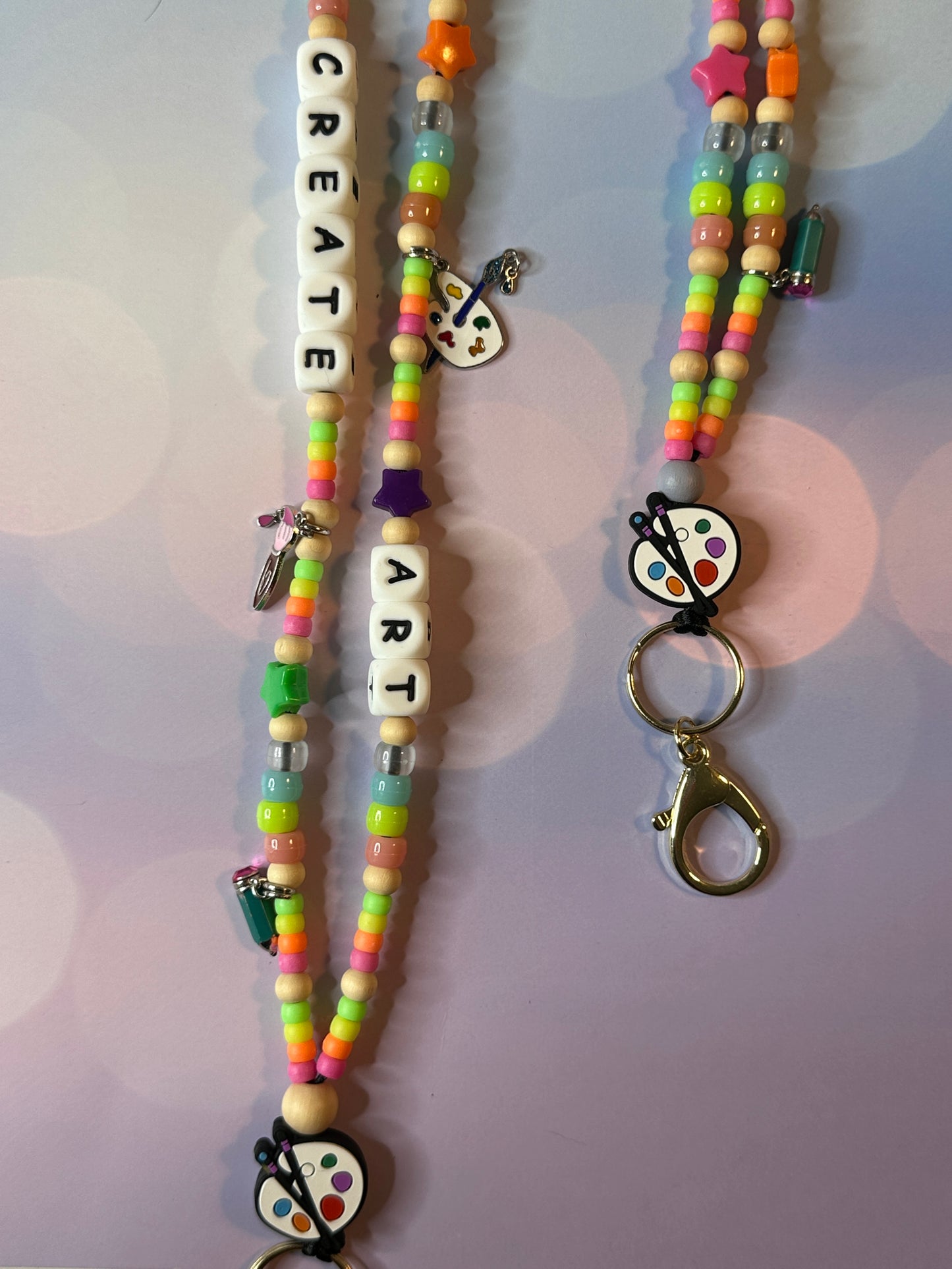 Two art teacher lanyards.  One lanyard is displaying the charms and colorful beads and the other is displaying the metal clasp.