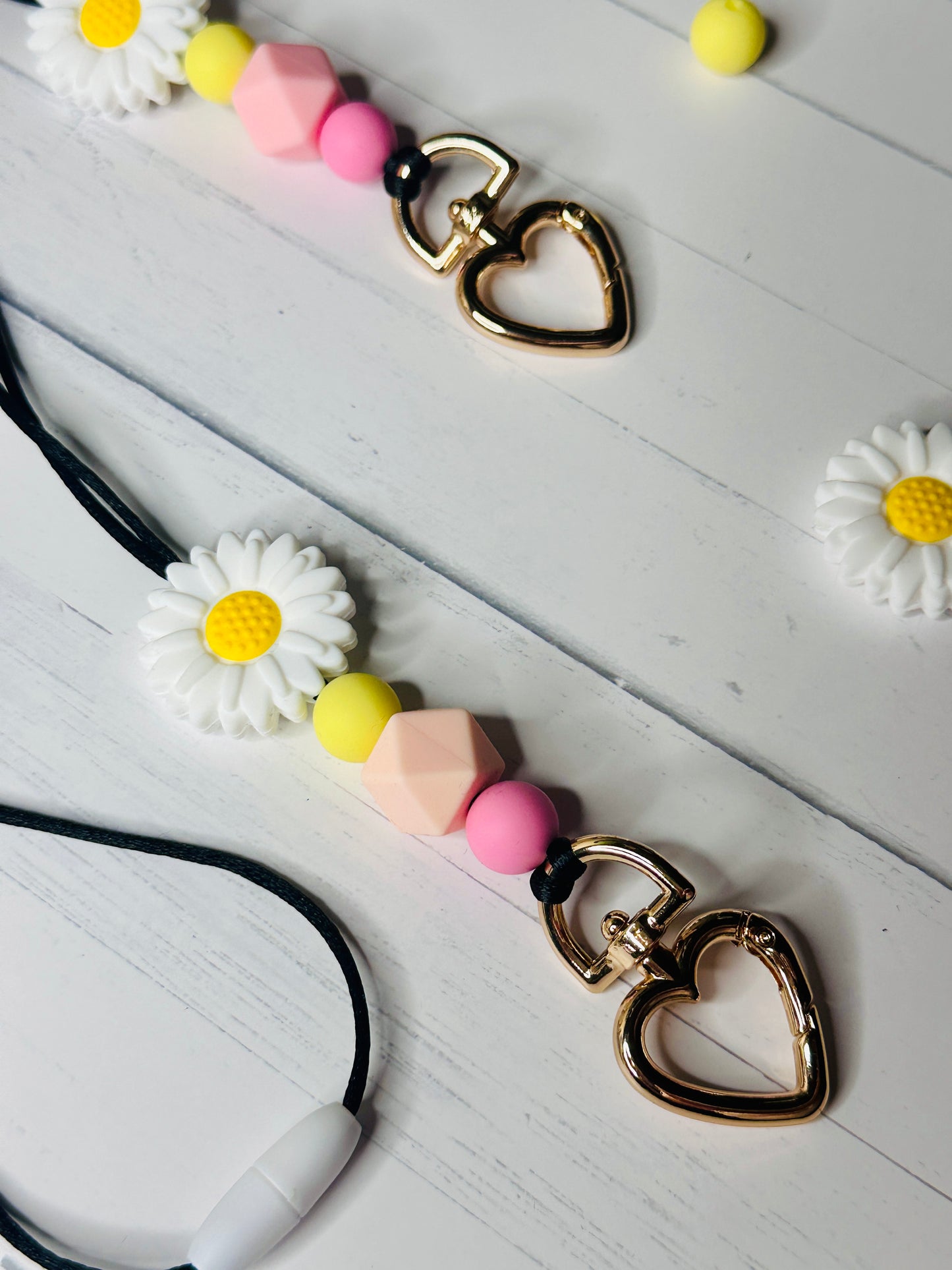 A close up view of the heart shaped metal clasp, daisy flower, and silicone beads on the Flower Lanyard.