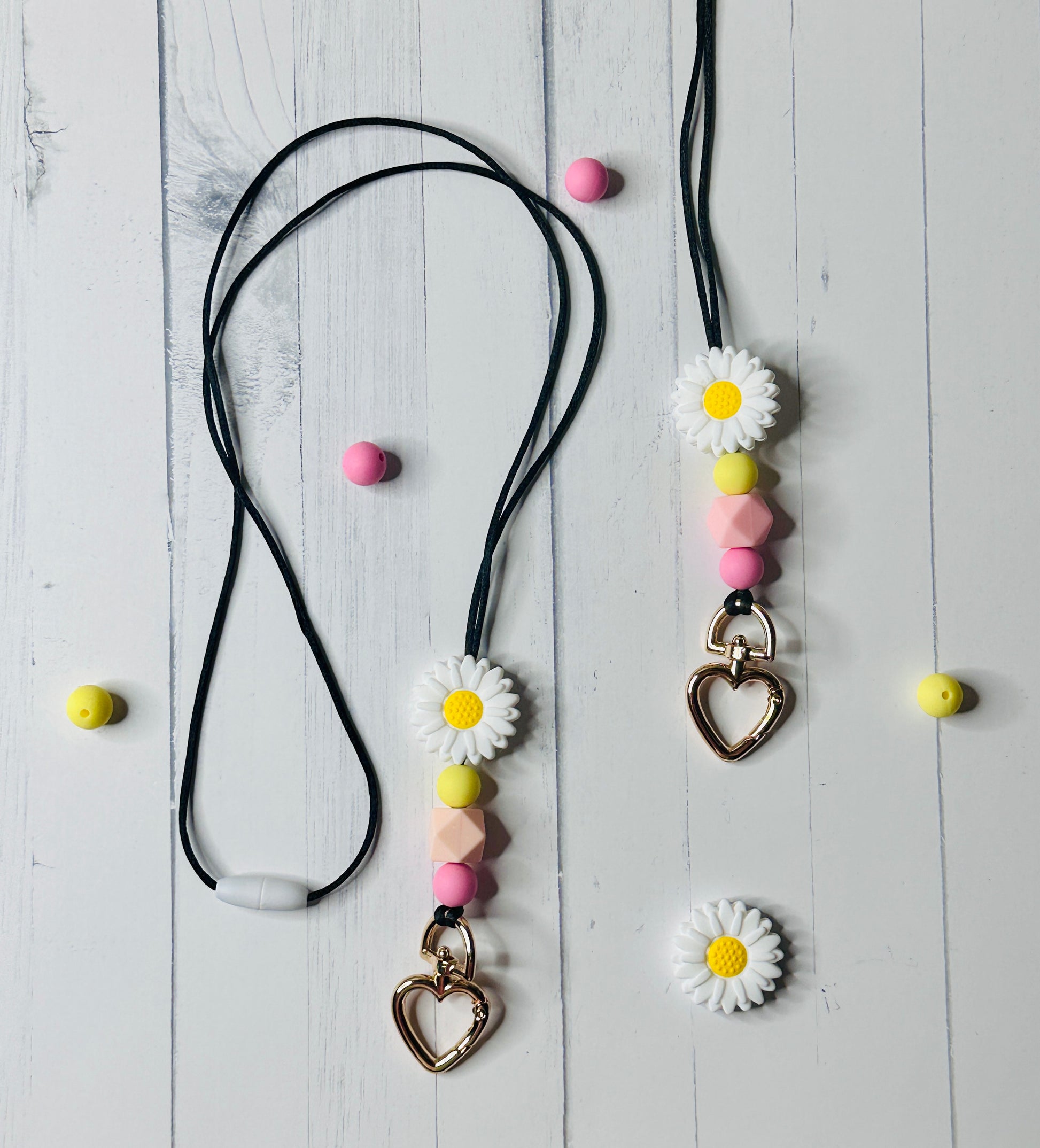 A wide view of the Flower Lanyards on a wooden table.  The clasps and silicon beads are displayed.  Silicon beads and daisy flower beads are scattered across the table.