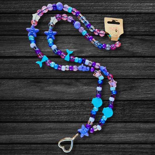 The Under The Sea Mermaid Lanyard on a dark black wooden background that contrasts the deep sea blue color of the beads.  Starfish, mermaid tails, seashells, and sea horse beads decorate this lanyard.